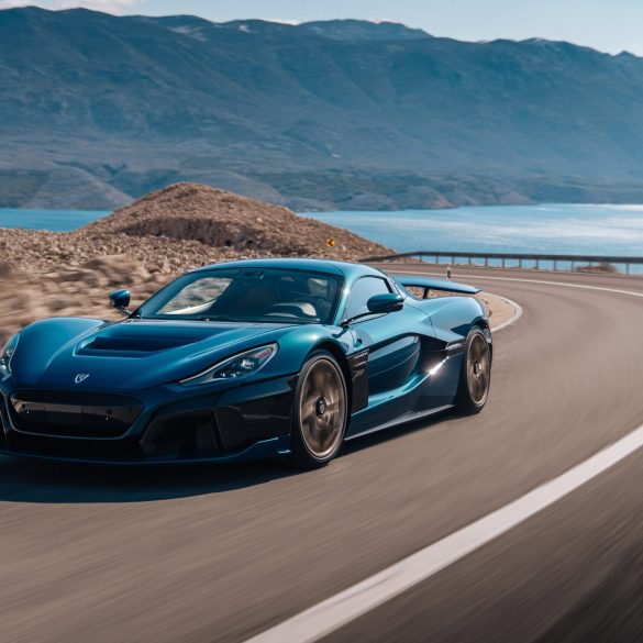 Navy blue Rimac Nevera speeding around curve on highway near water