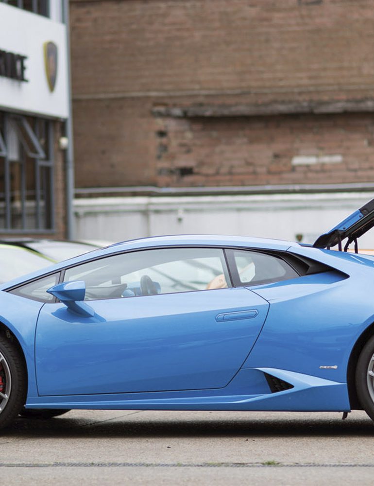 Man inspecting the engine bay of a blue Lamborghini Huracan