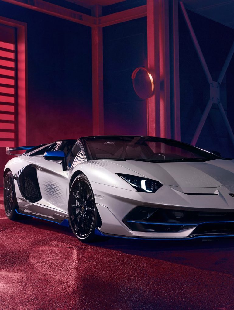 Front angled shot of a silver Lamborghini Aventador SVJ Roadster Xago Edition against a darkened background.