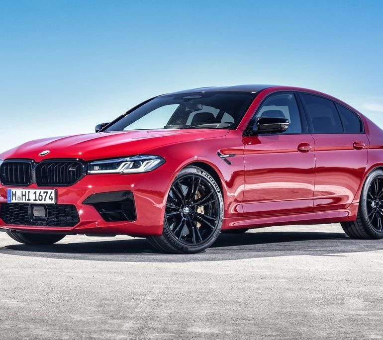 Front-angled view of a 2021 BMW M5 Competition finished in a bold red colour with orange undertones.