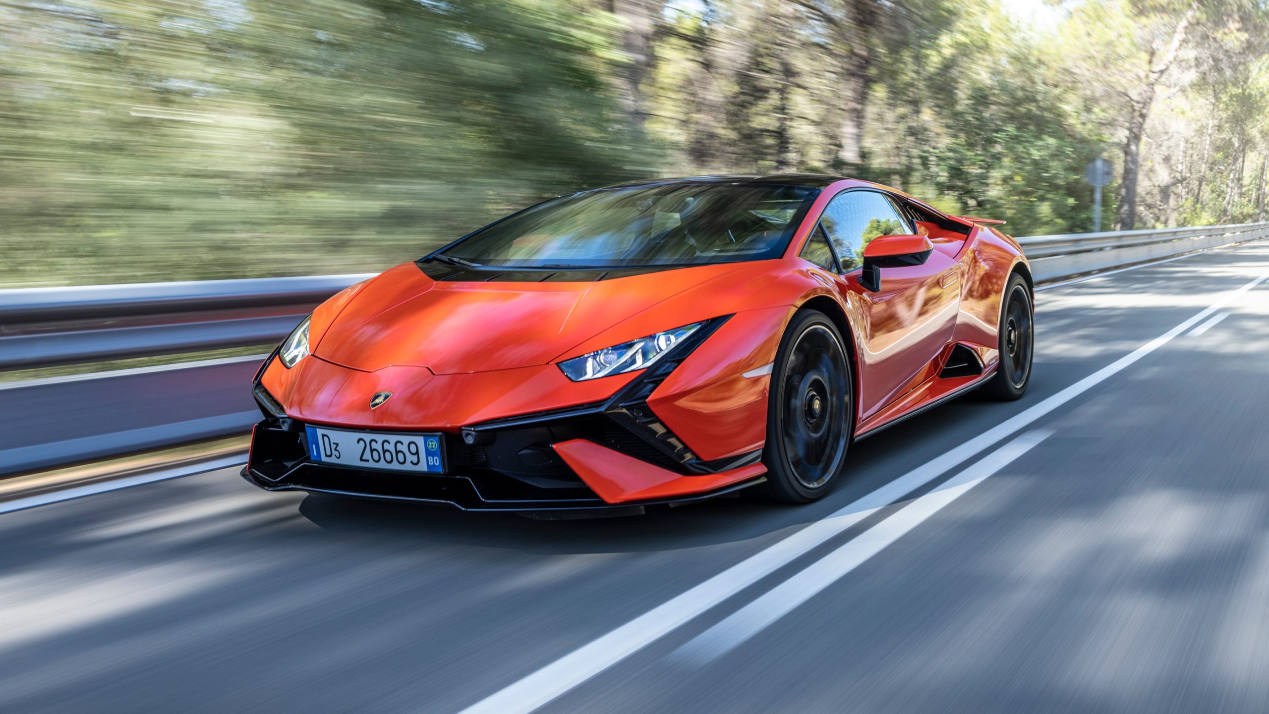 Front-angled view of an orange Lamborghini Tecnica rolling along a highway